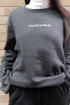 Goblin Suit: Ultra Cozy crewneck sweatshirt in dark grey with white 'CHAOS GOBLIN' text embroidered across chest, shown against brick wall background, displaying comfortable fleece material and relaxed fit design