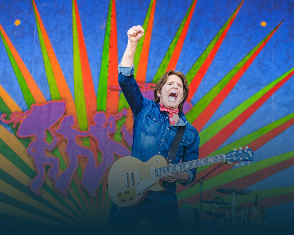 John Fogerty on stage with right hand in the air while playing the guitar. Photographed by Willow Haley