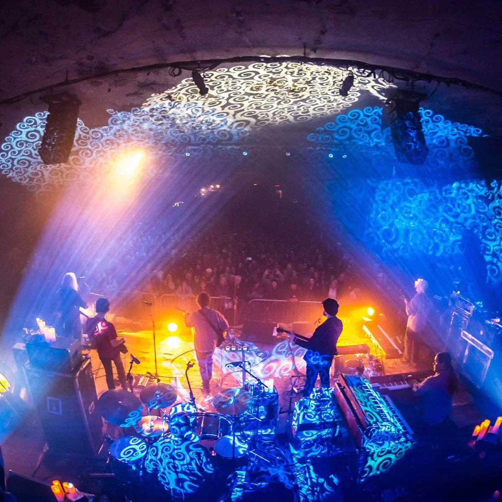 Railroad Earth playing on stage, and photographed from behind looking at the ground. Gold, blue and purple lighting tones illuminate the band. Photographed by Keith Griner,