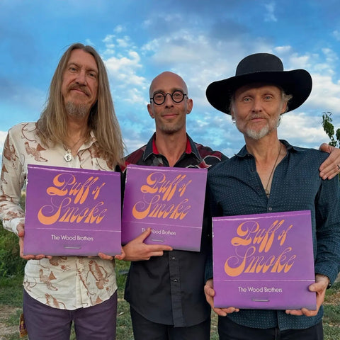 The Wood Brothers posing together against a blue sky all holding Puff of Smoke Vinyl 