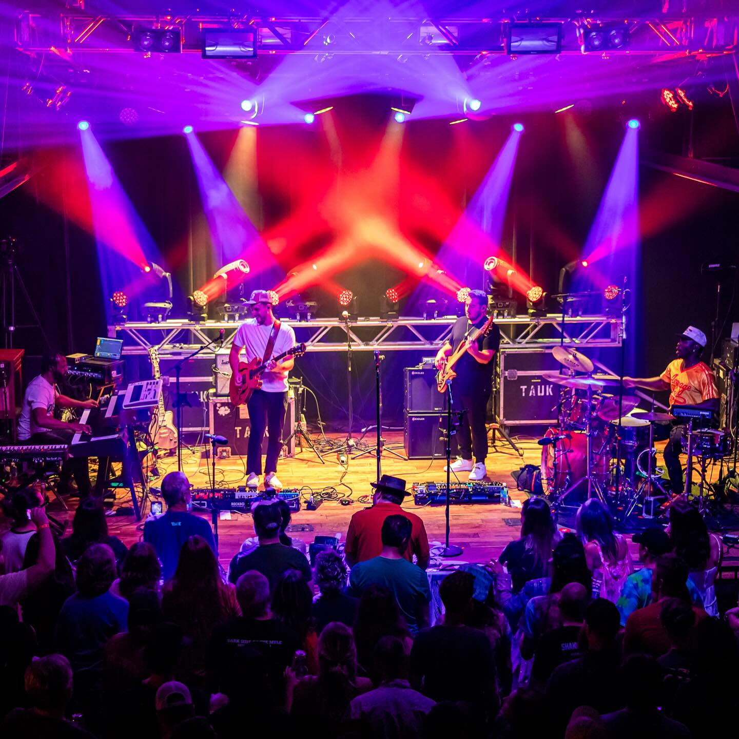 tauk on stage performing with view of the crowd and red and purple lighting