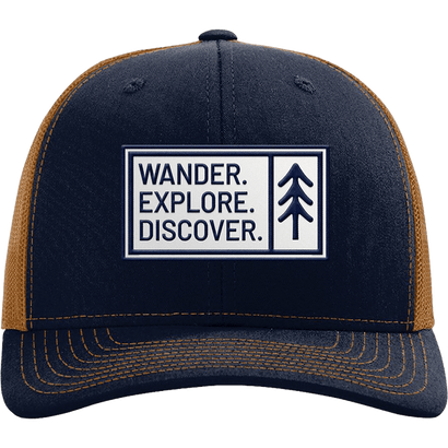 Navy and caramel trucker hat with structured front, mesh back, and patch reading Wander. Explore. Discover.