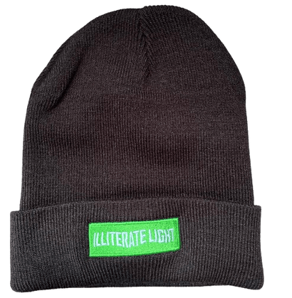 Dark knitted beanie with a folded cuff featuring a bright green rectangular patch with white text design