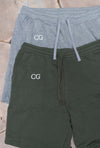 Goblin Suit with Shorts: Ultra Cozy shorts displayed in two colors - heather gray and forest green, featuring CG embroidered logo on upper right leg. Drawstring waistband shorts shown flat lay on wooden surface, highlighting comfortable casual design.
