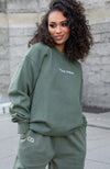 Green Goblin Jogger Set featuring an oversized fleece-lined crew neck sweatshirt with white Chaos Goblin embroidery and matching jogger pants. Comfortable unisex loungewear set shown in a sage green color against stone wall backdrop.