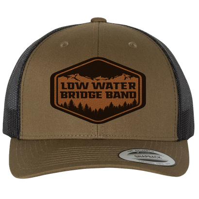 Coyote brown trucker hat with black mesh back featuring Low Water Bridge Band leather patch, outdoor-themed logo with mountains and trees, snapback closure for adjustable fit