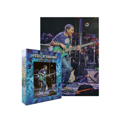 Limited edition 500-piece puzzle featuring a vibrant concert image of a bassist performing on stage, with the puzzle box displaying the same image and artist name Oteil Burbridge in bold text against a blue background