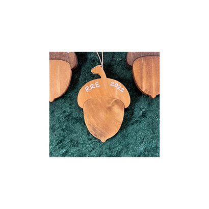 2022 RRE Christmas Ornament featuring a handcrafted wooden acorn design made from recycled Christmas trees, displaying natural woodgrain patterns on a deep green velvet background. The ornament is engraved with RRE 2022 on its surface.