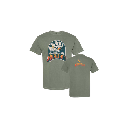 River Tee in moss green featuring a circular mountain river design with sun rays and a bird silhouette. Comfort Colors unisex t-shirt with front graphic print and small logo on back. Heavy-duty pre-shrunk cotton in earthy sage tone.