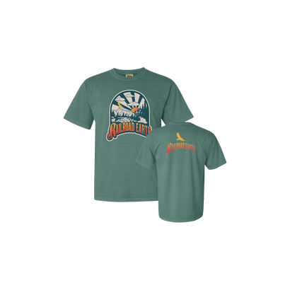 River Tee in light green features a circular mountain river design with a sunrise backdrop and flying bird detail. Front and back view of the comfort colors t-shirt showing nature-inspired artwork and brand logo in orange and blue tones on a sage green base.