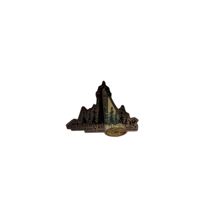 Limited edition 2014 Portland, ME Lighthouse Pin featuring a bronze-toned lighthouse silhouette rising above evergreen trees against a dark background, with decorative detailing inspired by The String Cheese Incident's artistic style. Collectible enamel pin with vintage aesthetic.