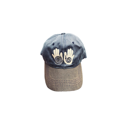 Little Hands Hat in navy blue with brown bill, featuring white embroidered spiral hand designs on the front. Classic baseball cap style with contrast stitching detail.