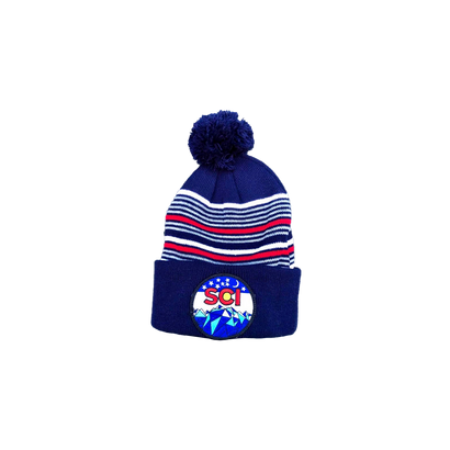 SCI Patch Beanie featuring a navy blue knit design with white and red striped pattern, topped with a matching pom-pom. The beanie displays the iconic SCI logo patch with mountain scenery against a folded brim.